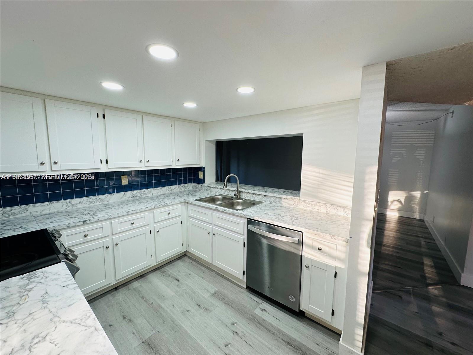 A kitchen features white cabinets, marble-patterned countertops, a blue tiled backsplash, and stainless steel appliances — 9501 Seagrape Dr # 101, Davie FL 33324, DAVIE, FL