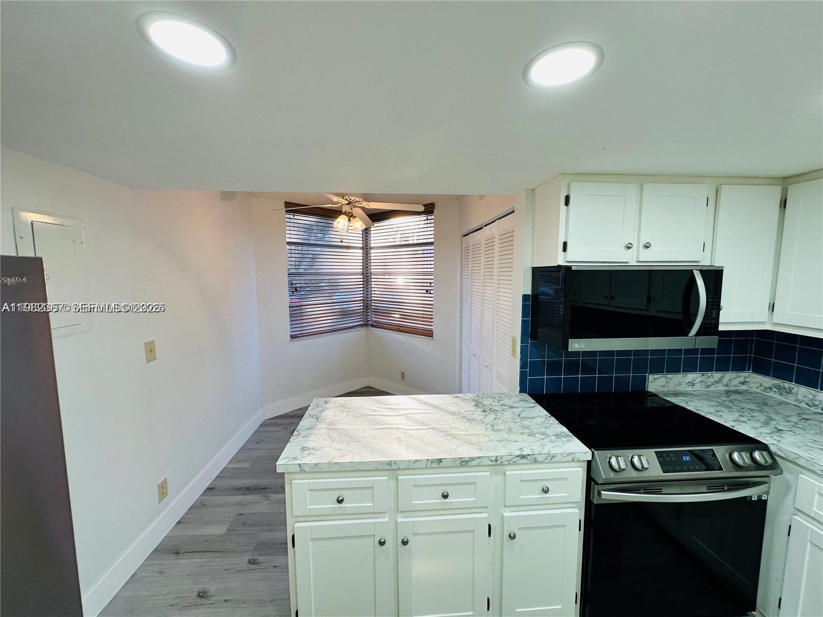 A kitchen features white cabinets, a marble-patterned island, and a corner window with blinds — 9501 Seagrape Dr # 101, Davie FL 33324, DAVIE, FL