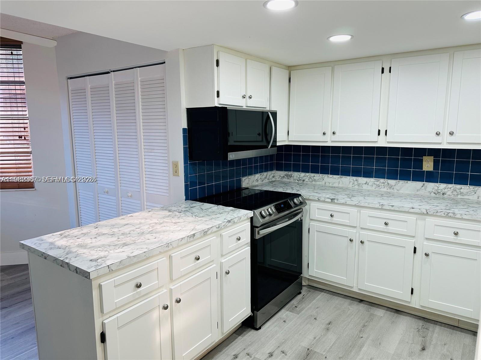 A kitchen features white cabinets, marble-patterned countertops, a blue tiled backsplash, and stainless appliances — 9501 Seagrape Dr # 101, Davie FL 33324, DAVIE, FL