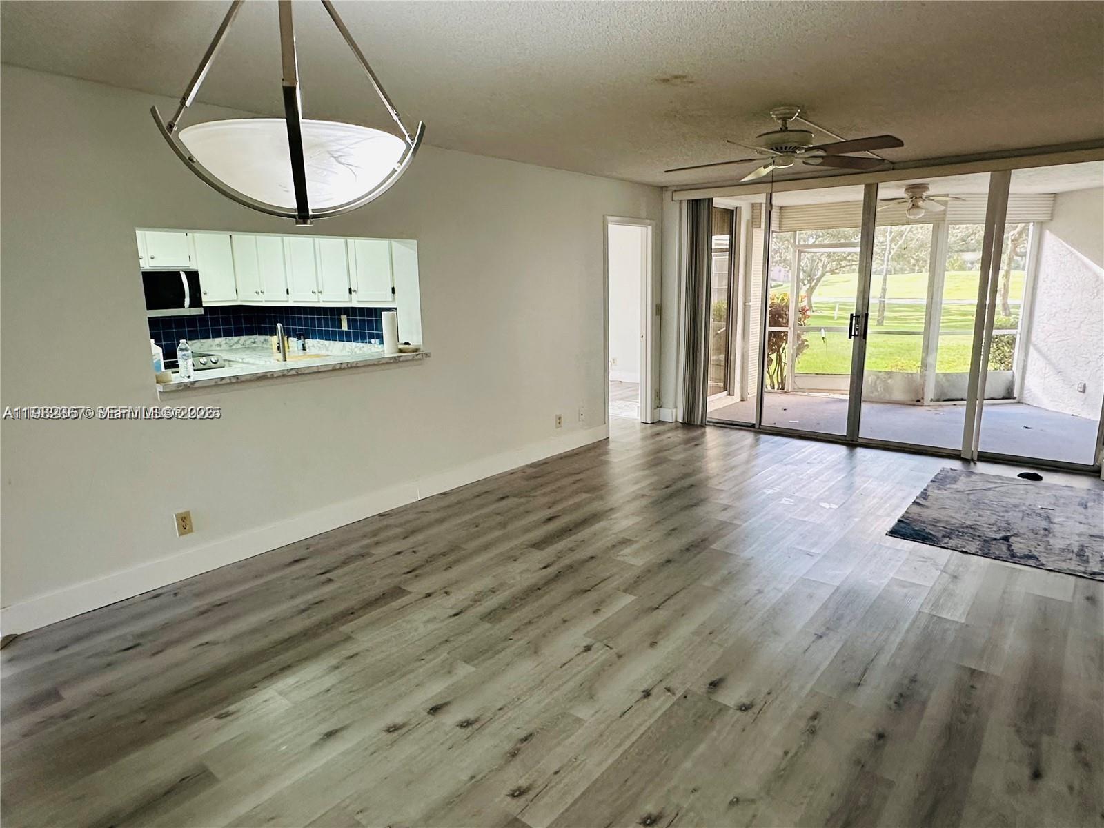 This living room features light wood-look flooring, a kitchen pass-through, and sliding glass doors — 9501 Seagrape Dr # 101, Davie FL 33324, DAVIE, FL
