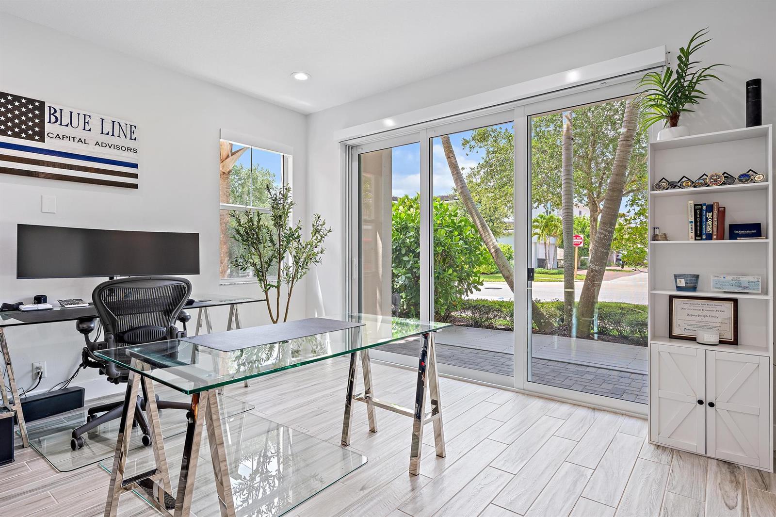 A home office features a glass desk, an ergonomic chair, and sliding doors to a patio — 4145 Faraday Way, Palm Beach Gardens FL 33418, PALM BEACH GARDENS, FL