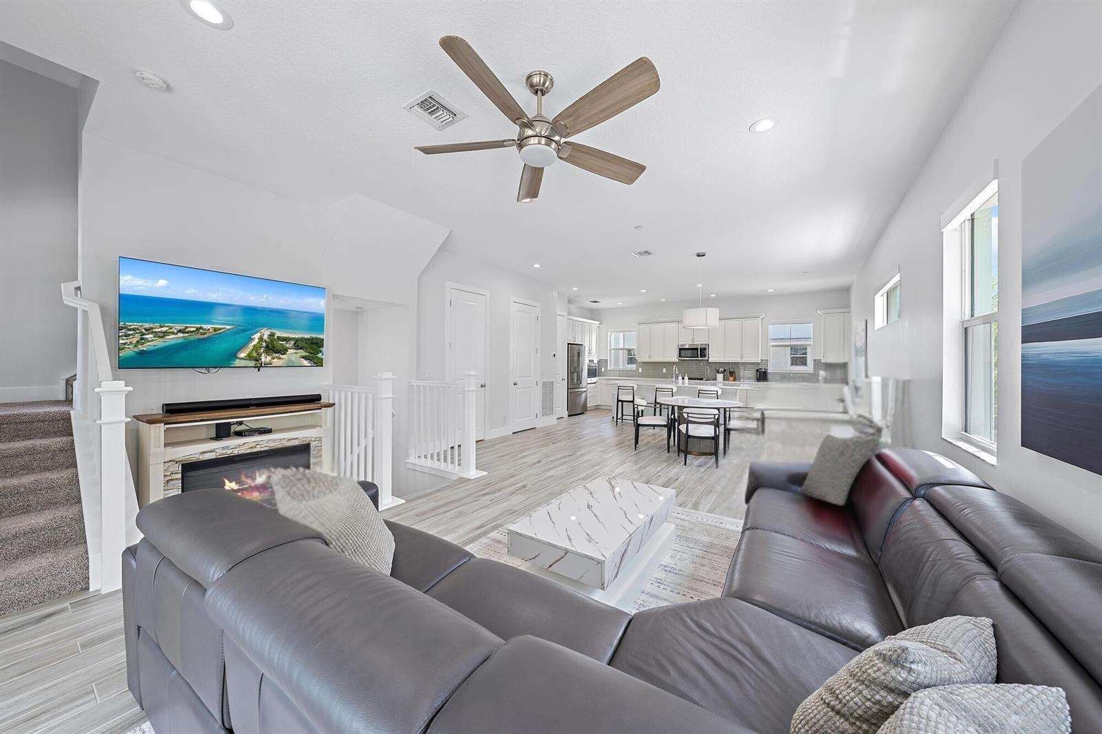 A living room with a grey sectional, fireplace, and television opens to a white kitchen — 4145 Faraday Way, Palm Beach Gardens FL 33418, PALM BEACH GARDENS, FL