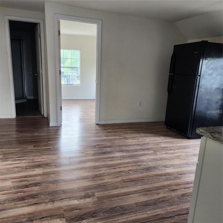 A room with wood-look flooring, a black refrigerator, and two doorways leading to other spaces — 1414 MINNESOTA AVENUE UNIT B, ST CLOUD, FL
