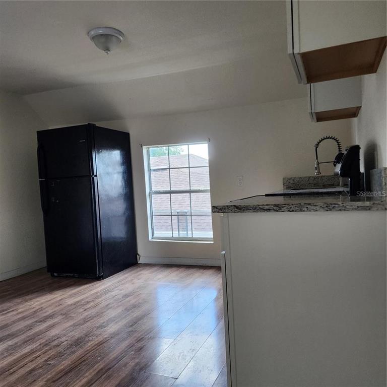 A kitchen with wood-look flooring, a black refrigerator, white cabinets, and granite countertops — 1414 MINNESOTA AVENUE UNIT B, ST CLOUD, FL