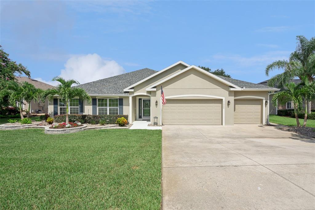 A single-story house with a beige stucco exterior, a three-car garage, and a landscaped lawn — 11332 LITTLE NELLIE DRIVE, CLERMONT, FL
