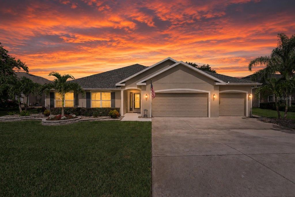 A single-story house with a three-car garage and a landscaped front yard at sunset — 11332 LITTLE NELLIE DRIVE, CLERMONT, FL