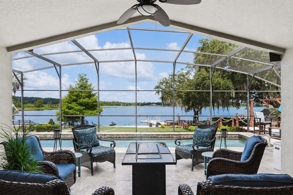 A covered patio with wicker furniture overlooks a swimming pool and a lake beyond — 11332 LITTLE NELLIE DRIVE, CLERMONT, FL