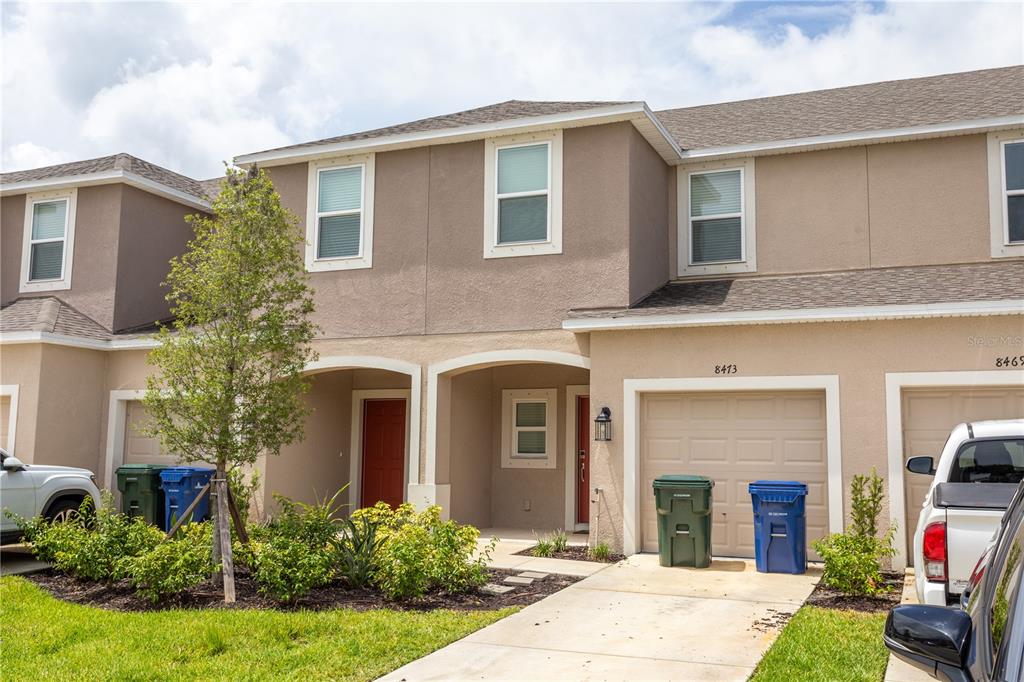 A two-story townhouse exterior features tan stucco walls, a garage, and a small front yard — 8473 LUNAR SKYE STREET, SARASOTA, FL