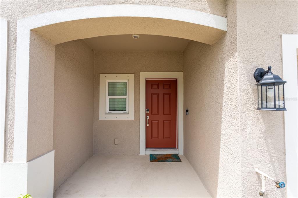 A covered entryway features a red front door, a small window, and a wall lantern — 8473 LUNAR SKYE STREET, SARASOTA, FL