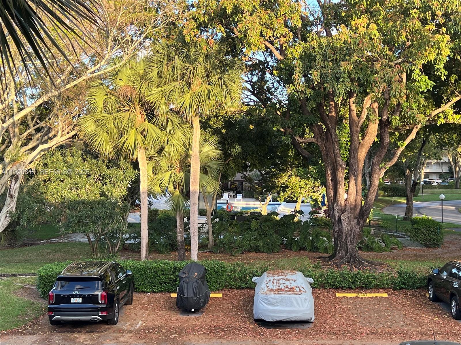 A parking lot with several vehicles sits in front of a pool area and trees — 907 Cypress Ter # 203, Pompano Beach FL 33069, POMPANO BEACH, FL
