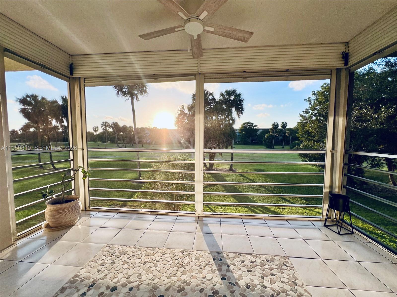 A screened-in balcony with tiled flooring overlooks a golf course at sunset — 907 Cypress Ter # 203, Pompano Beach FL 33069, POMPANO BEACH, FL