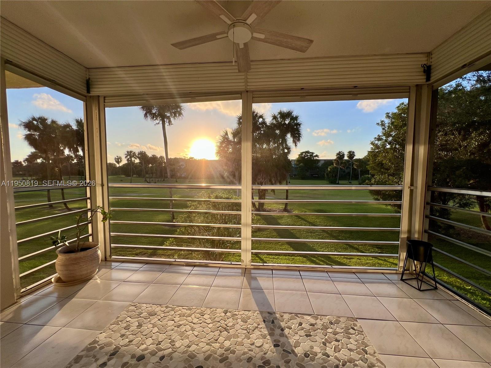 A screened-in porch with tiled flooring overlooks a grassy golf course at sunset — 907 Cypress Ter # 203, Pompano Beach FL 33069, POMPANO BEACH, FL