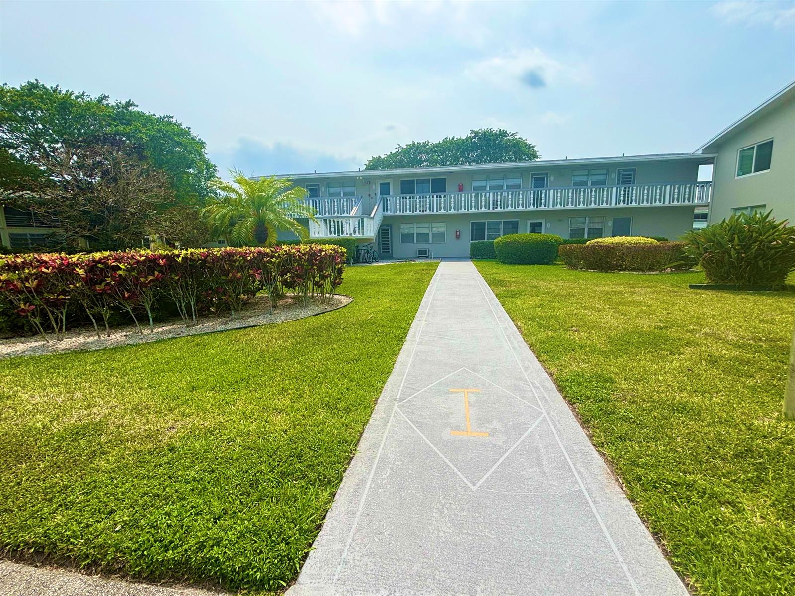 A concrete walkway leads to the entrance of a two-story apartment building with balconies — 203 Farnham I # 203, Deerfield Beach FL 33442, DEERFIELD BEACH, FL