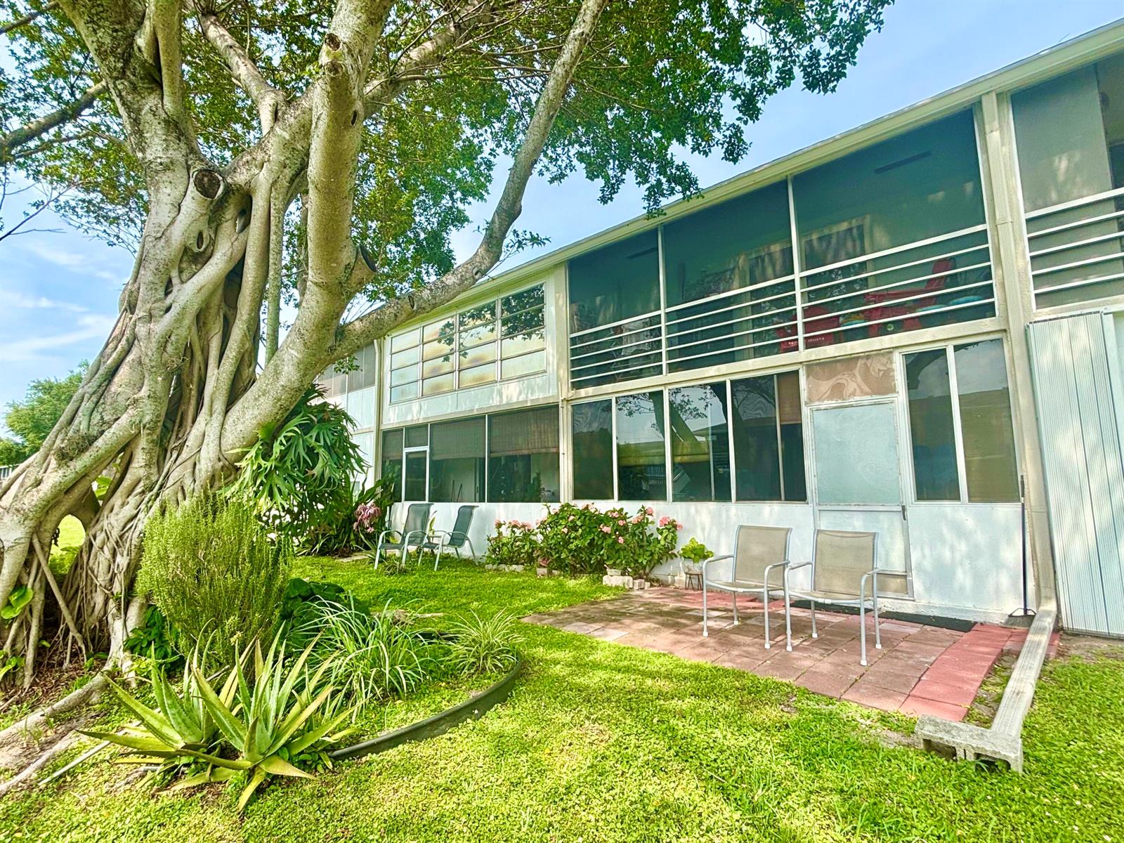 A two-story building with screened balconies sits beside a large tree and a patio — 203 Farnham I # 203, Deerfield Beach FL 33442, DEERFIELD BEACH, FL