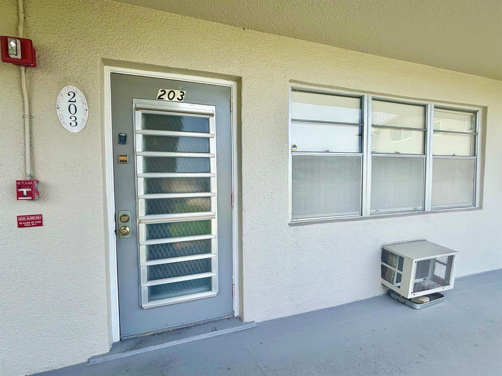 An exterior view of a residential unit entrance featuring a grey door and window — 203 Farnham I # 203, Deerfield Beach FL 33442, DEERFIELD BEACH, FL