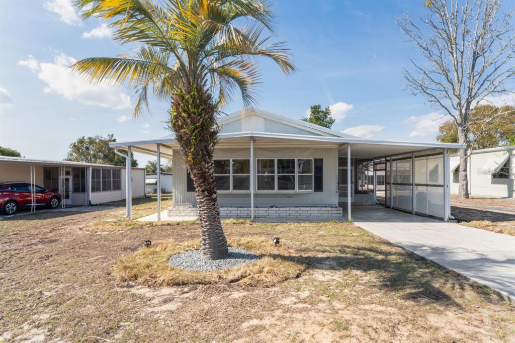A single-story manufactured home features a palm tree in the front yard and a carport — 15071 RIALTO AVENUE, BROOKSVILLE, FL