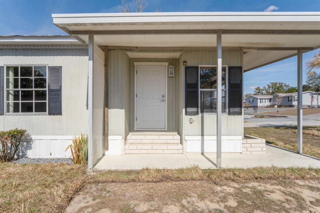 The exterior of a manufactured home features a covered porch, white door, and shuttered windows — 15071 RIALTO AVENUE, BROOKSVILLE, FL