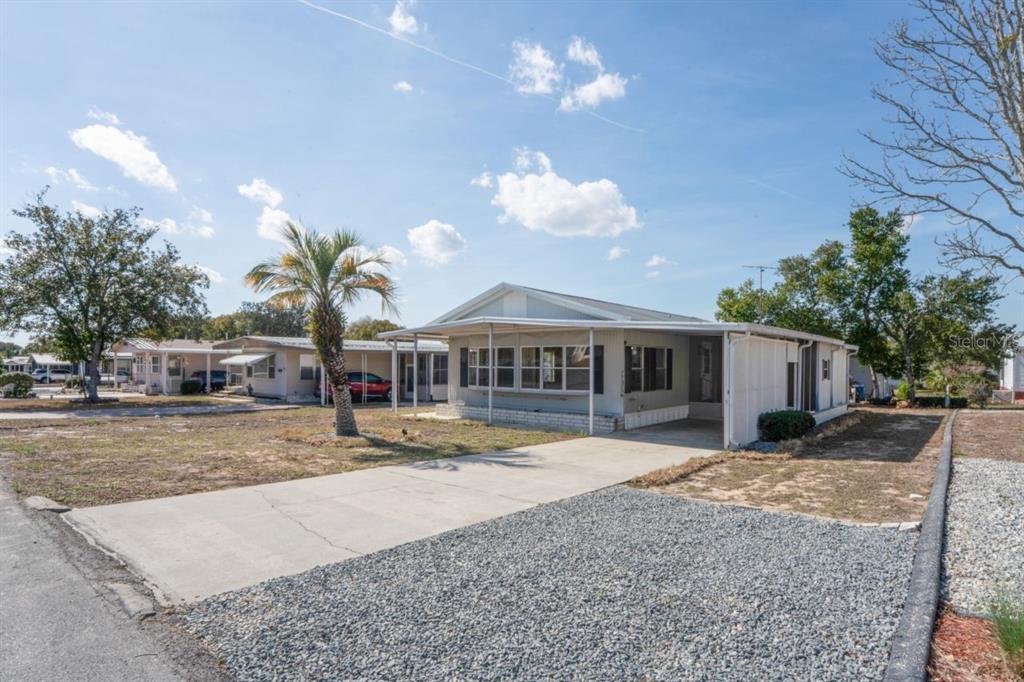 A light-colored mobile home with a concrete driveway and a covered carport under a blue sky — 15071 RIALTO AVENUE, BROOKSVILLE, FL