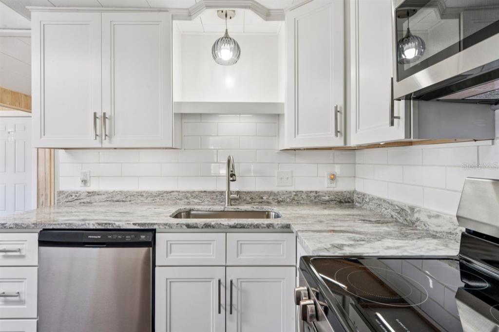 A kitchen featuring white cabinets, granite countertops, a stainless steel dishwasher, and a subway tile backsplash — 15071 RIALTO AVENUE, BROOKSVILLE, FL
