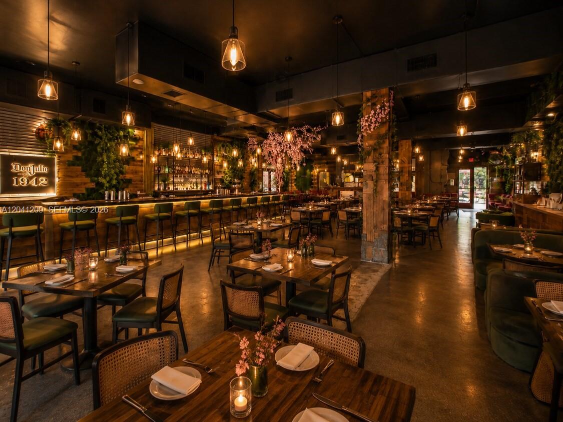 A dimly lit restaurant interior featuring wooden tables, green chairs, and hanging pendant lights — 3023 Biscayne Blvd, Miami FL 33137, MIAMI, FL