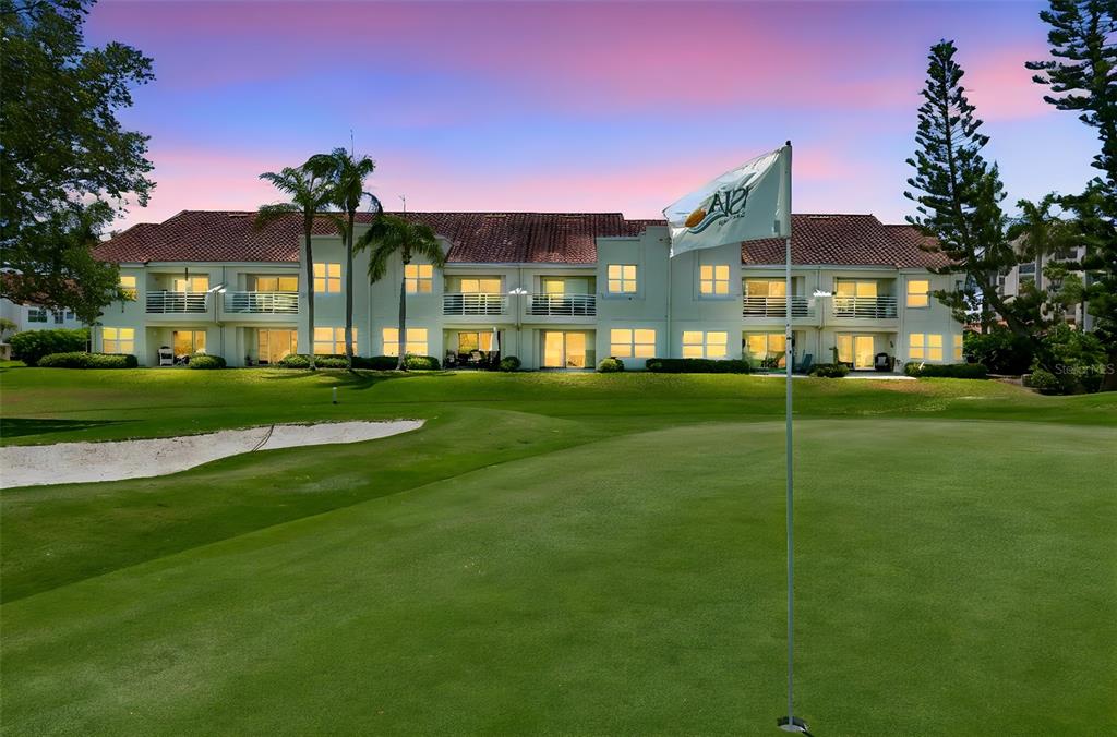 A golf course green with a flagstick sits in front of a multi-story apartment building — 6085 BAHIA DEL MAR BOULEVARD UNIT 106, ST PETERSBURG, FL