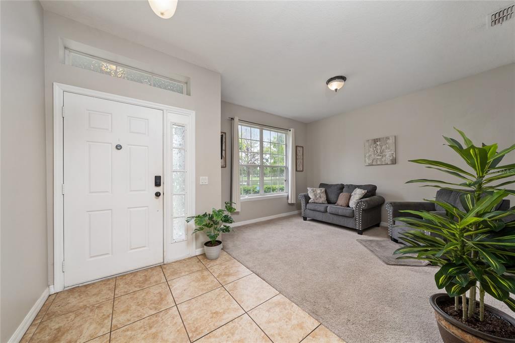 An entryway with tile flooring leads into a carpeted living area featuring a gray sofa — 3108 WESTBROOK ROAD, KISSIMMEE, FL