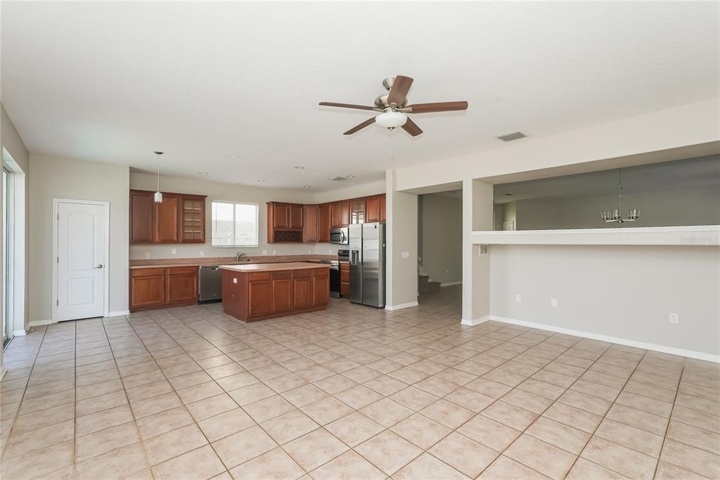 A kitchen with wood cabinets, a center island, and tile flooring opens to a living area — 12125 FOX BLOOM AVENUE, GIBSONTON, FL