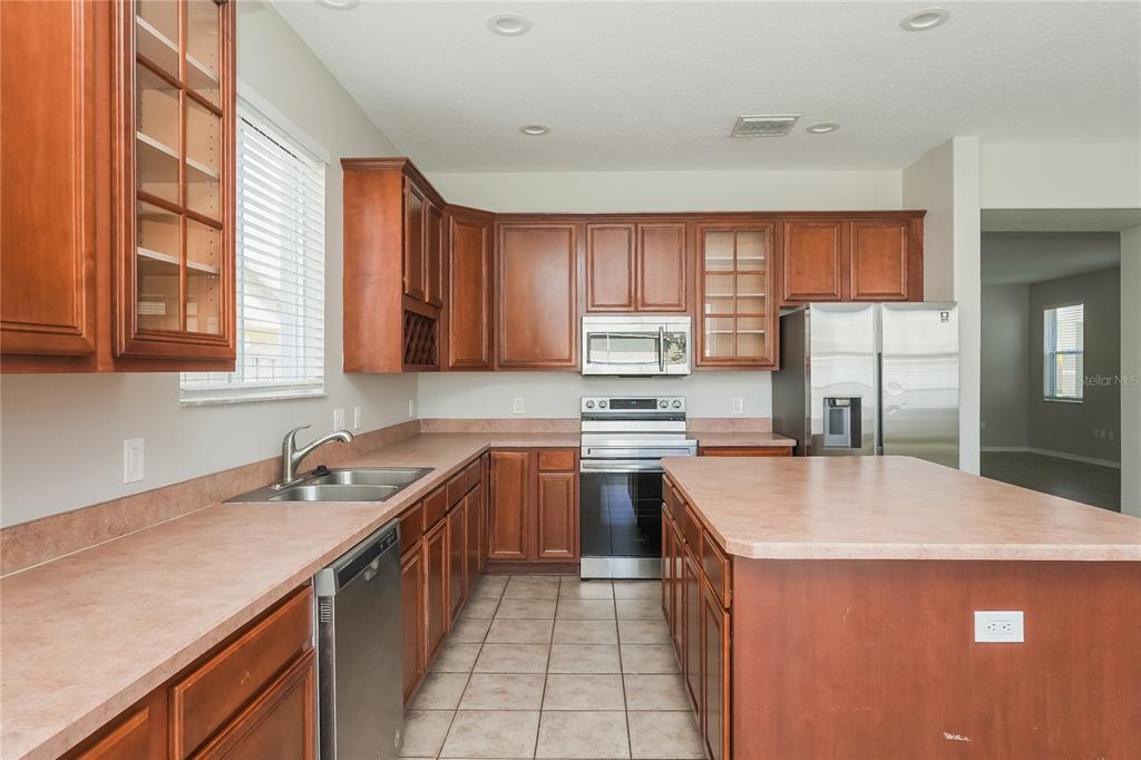A kitchen features wood cabinets, laminate countertops, stainless steel appliances, and tile flooring — 12125 FOX BLOOM AVENUE, GIBSONTON, FL
