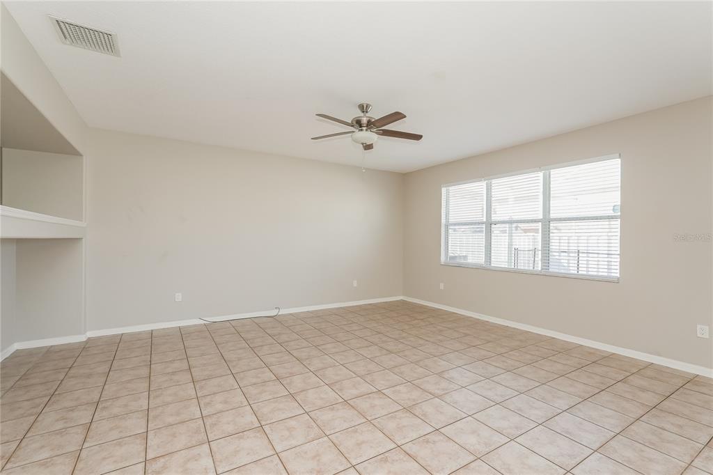 An empty room features beige tile flooring, light-colored walls, a ceiling fan, and large windows — 12125 FOX BLOOM AVENUE, GIBSONTON, FL