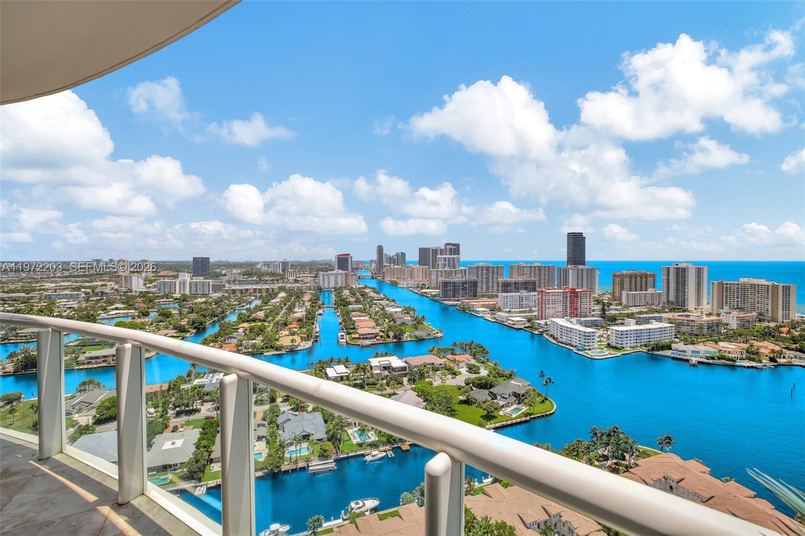 A high-angle view from a balcony overlooking a canal, residential properties, and a distant skyline — 21200 Point Pl, Aventura FL 33180, AVENTURA, FL
