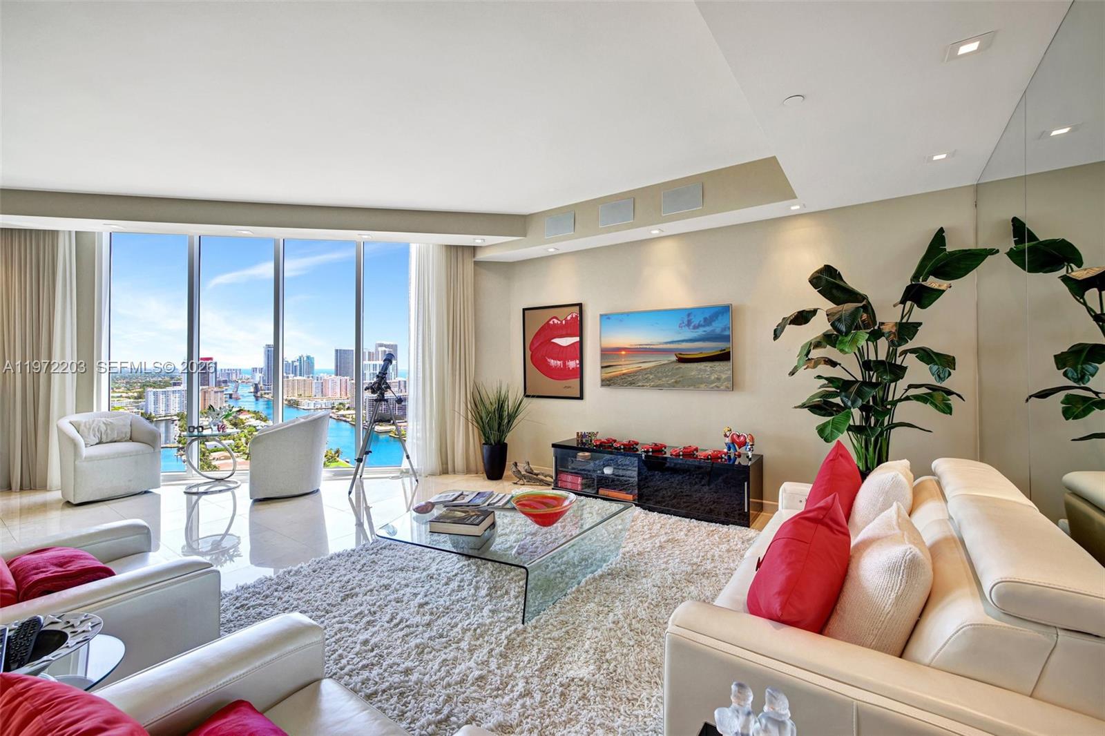 A modern living room features a glass coffee table, white sofa, and floor-to-ceiling windows — 21200 Point Pl, Aventura FL 33180, AVENTURA, FL