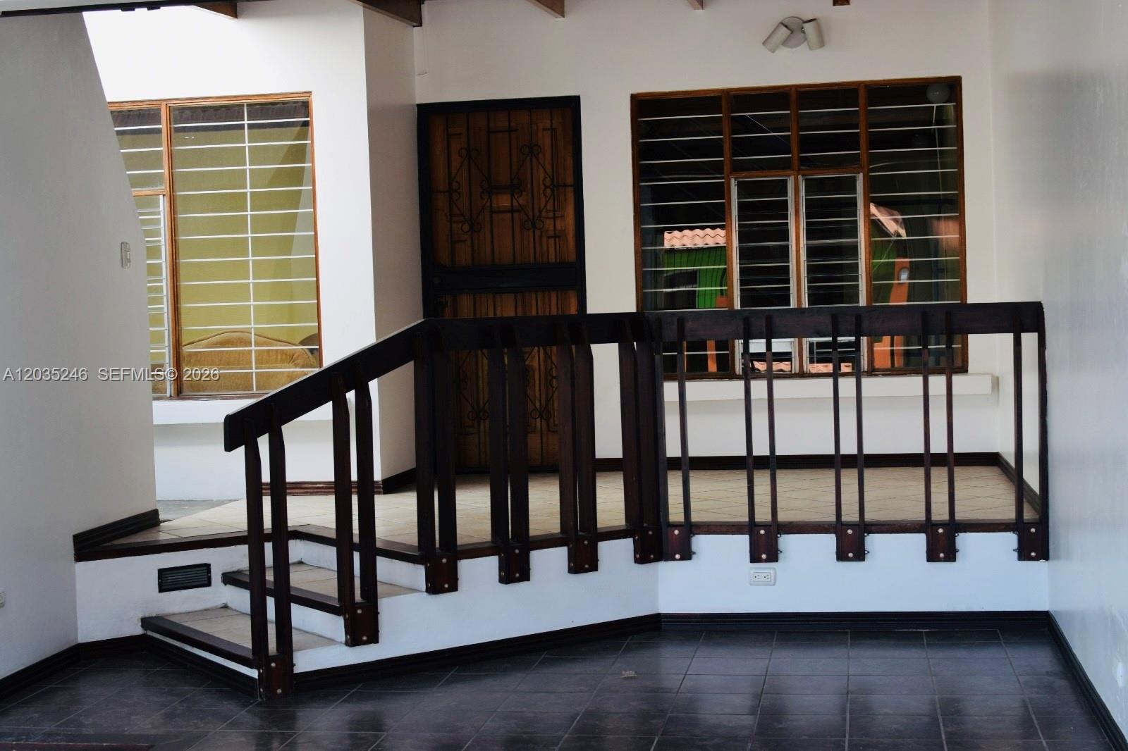 A raised porch with dark wood railings and stairs leads to a front door and windows — Cartago Cartago, FL, FL