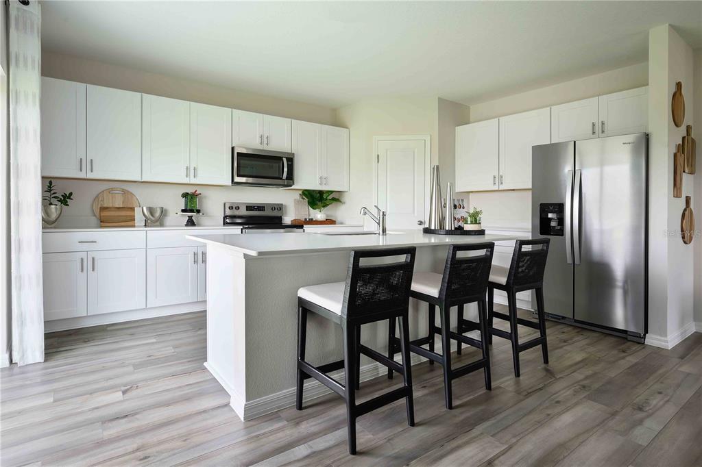 A modern kitchen features white cabinetry, a central island with bar seating, and stainless appliances — 33661 NOBLE CREEK PLACE, DADE CITY, FL