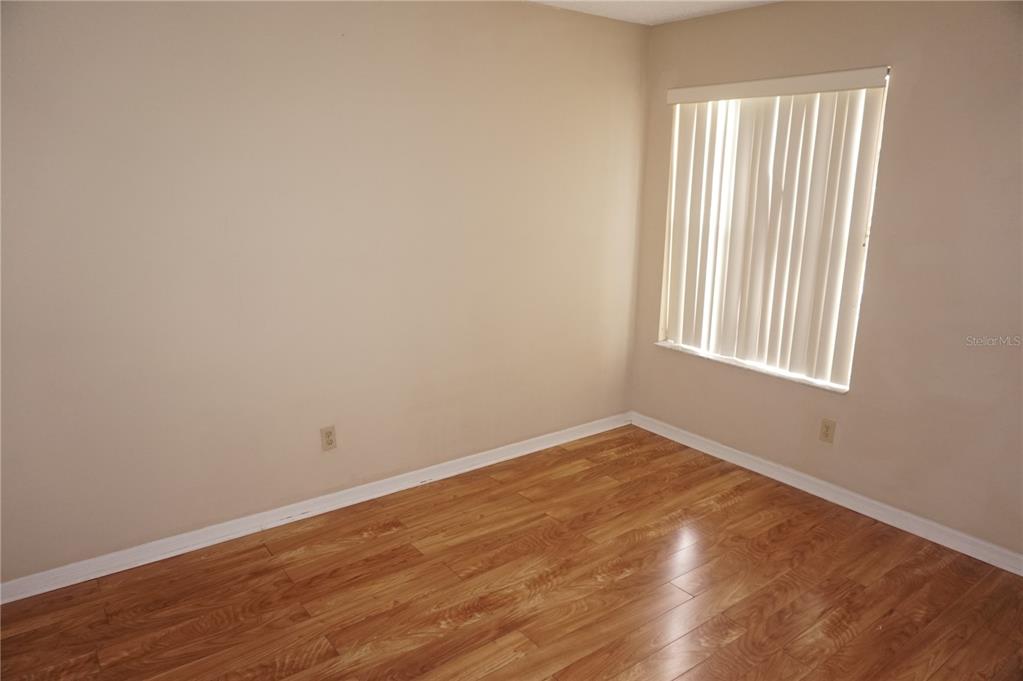 An empty room features light-colored walls, wood-look laminate flooring, and a window with vertical blinds — 2749 N POINCIANA BOULEVARD UNIT 24, KISSIMMEE, FL