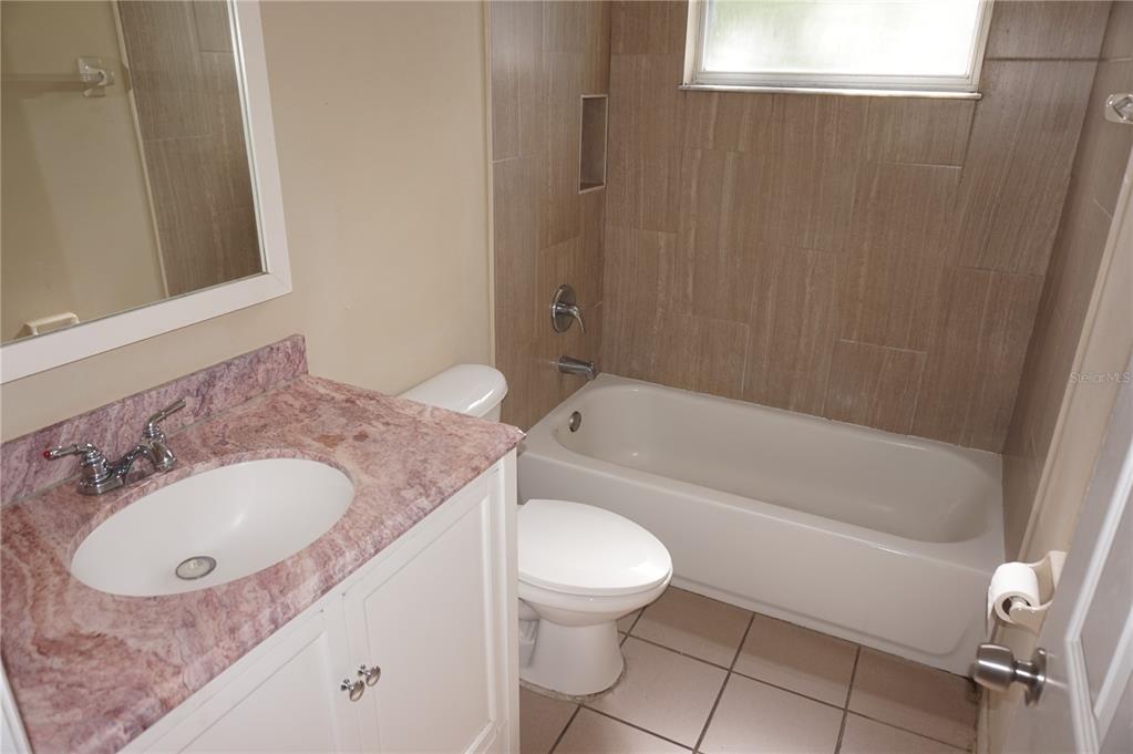 A bathroom features a white vanity with a pink marble countertop, toilet, and tiled tub — 2749 N POINCIANA BOULEVARD UNIT 24, KISSIMMEE, FL