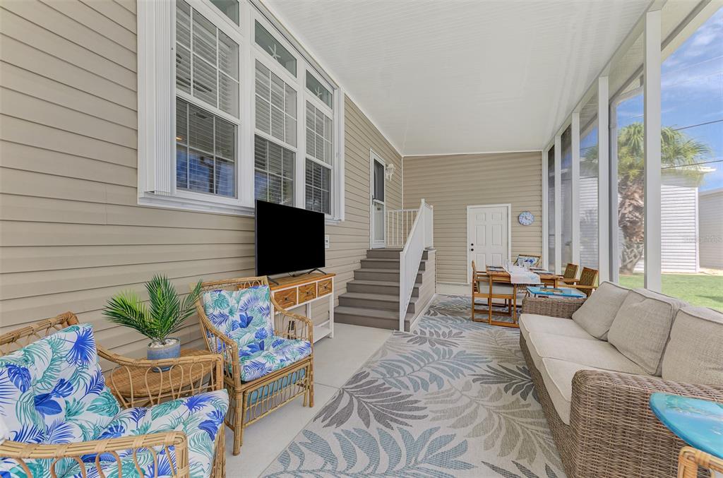 A screened-in porch features wicker furniture, a television, and a dining set on a rug — 804 TURF, VENICE, FL