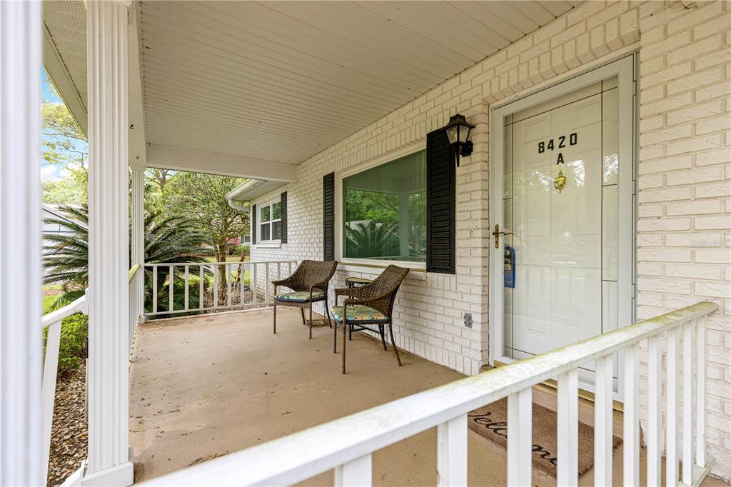 A covered front porch features white brick walls, two wicker chairs, and a white door — 8420 SW 92ND STREET UNIT A, OCALA, FL