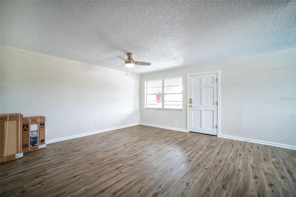 An empty room with light-colored walls, wood-look flooring, a ceiling fan, and a front door — 6062 22ND AVENUE N UNIT 5, ST PETERSBURG, FL