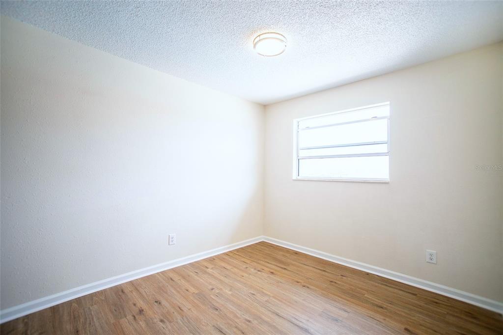 An empty bedroom features light-colored walls, wood-look flooring, a ceiling light, and a window — 6062 22ND AVENUE N UNIT 5, ST PETERSBURG, FL
