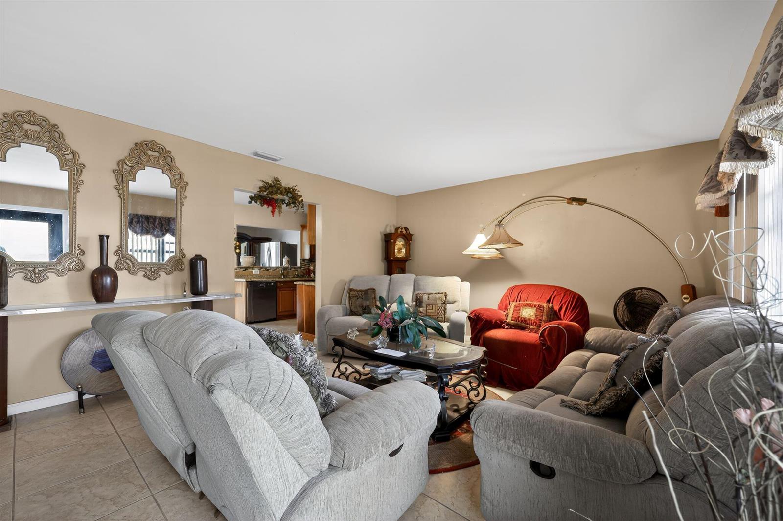 A living room with gray reclining sofas, a red armchair, and two ornate wall mirrors — 9522 Affirmed Lane, Boca Raton FL 33496, BOCA RATON, FL