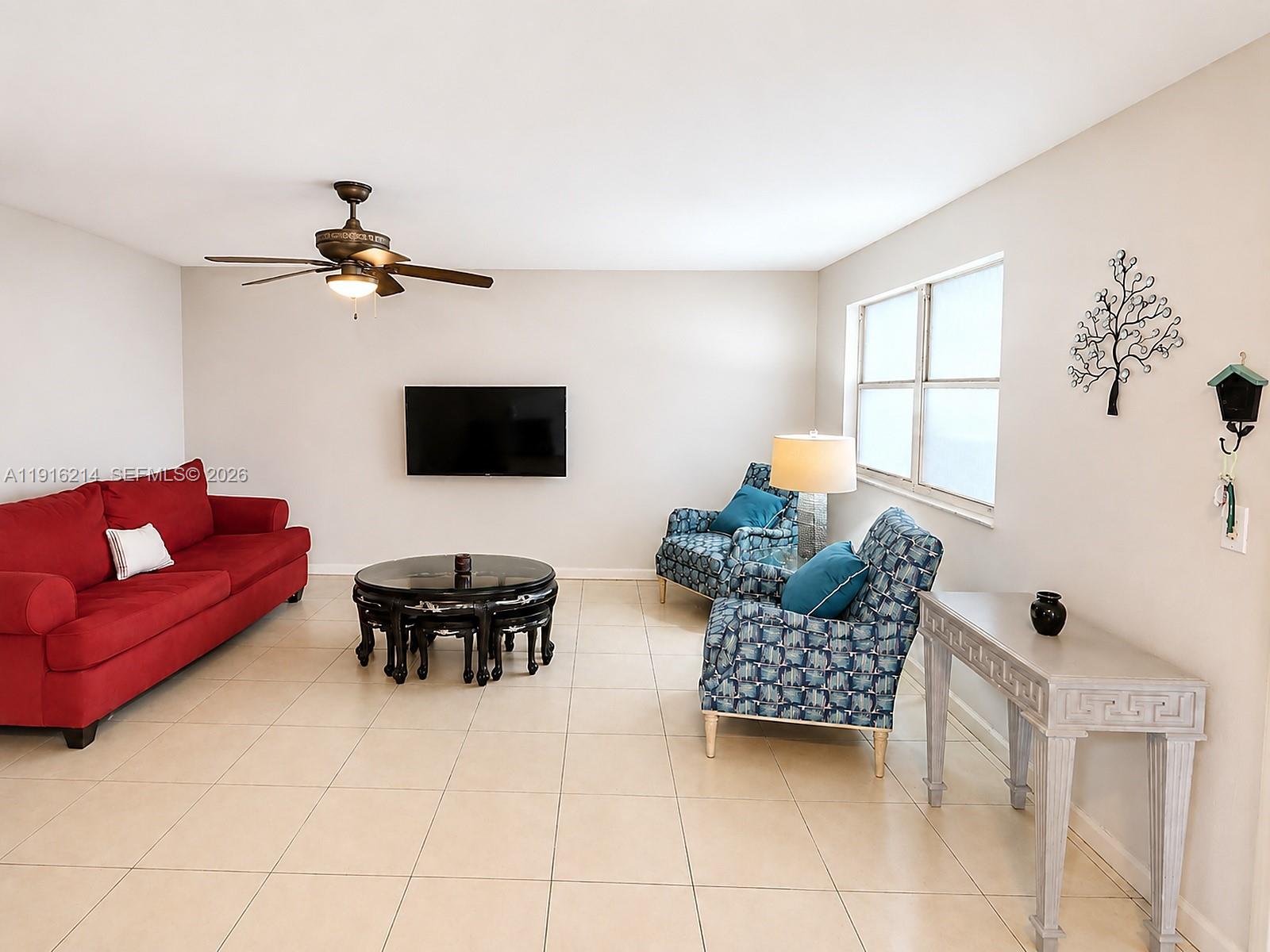 A living room features a red sofa, two patterned armchairs, a coffee table, and television — 116 Tuscany B # 116, Delray Beach FL 33446, DELRAY BEACH, FL