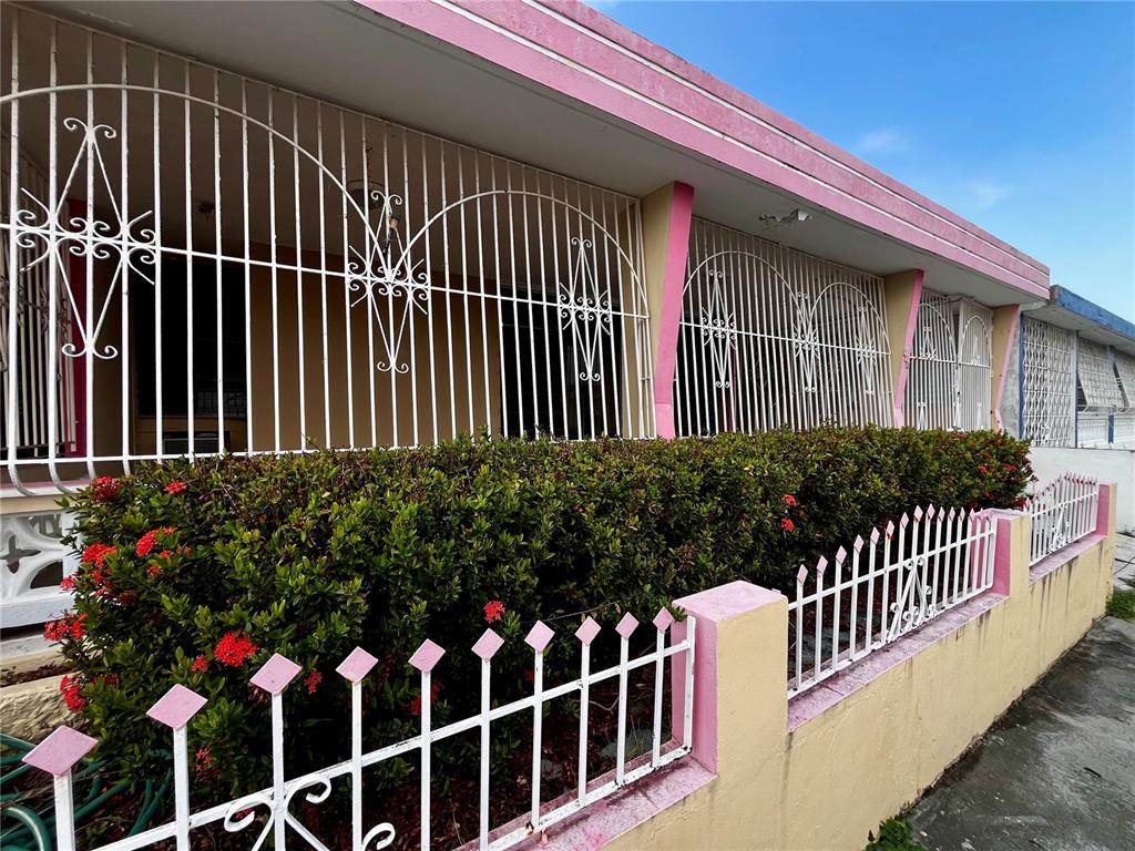 A pink house exterior features white metal security bars over the windows and a low fence — Urb Santa Isidra 2 #130, FAJARDO, PR