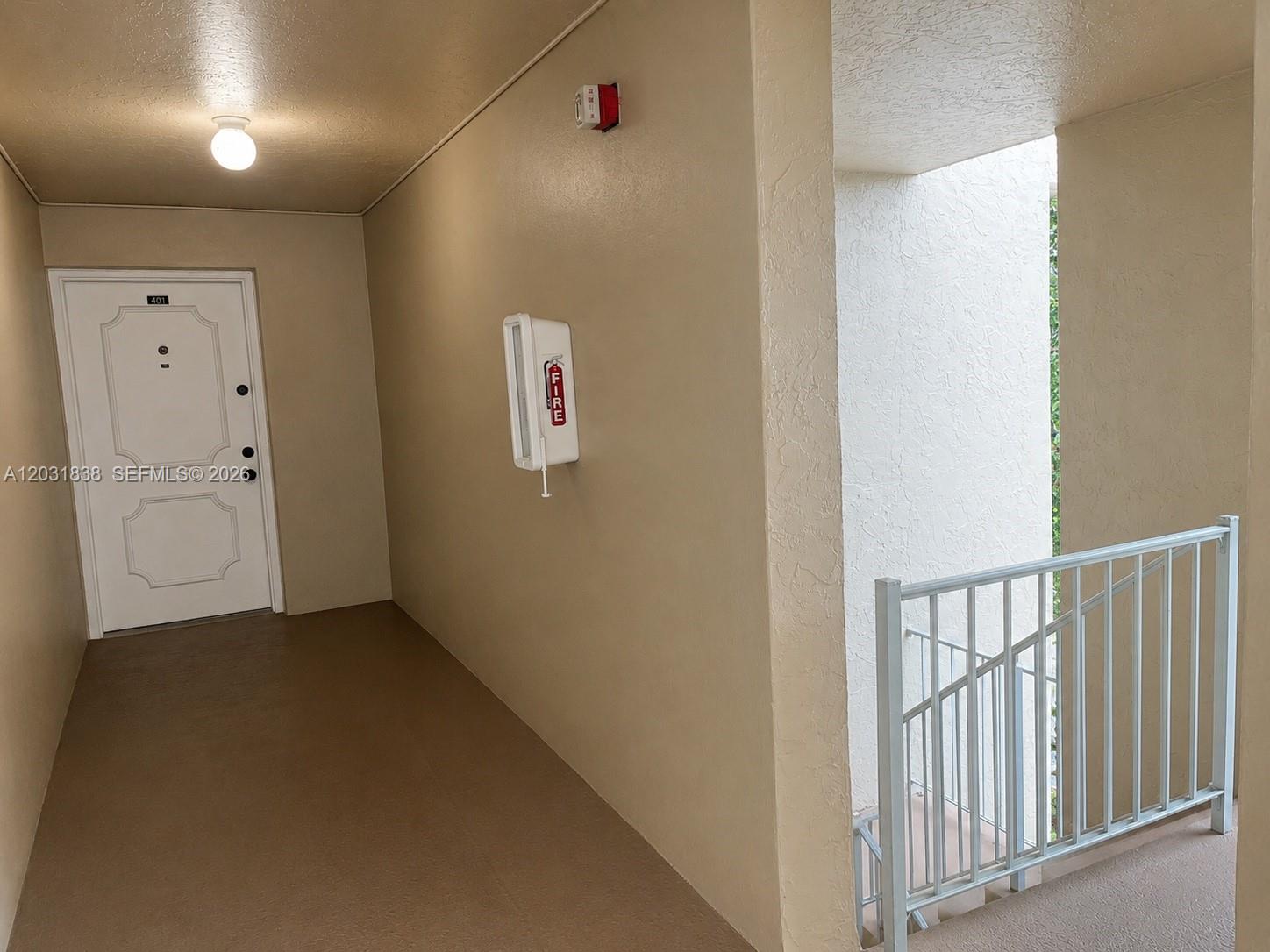 An apartment hallway features a white door, a fire extinguisher cabinet, and a metal railing — 9420 Tangerine Pl # 401, Davie FL 33324, DAVIE, FL