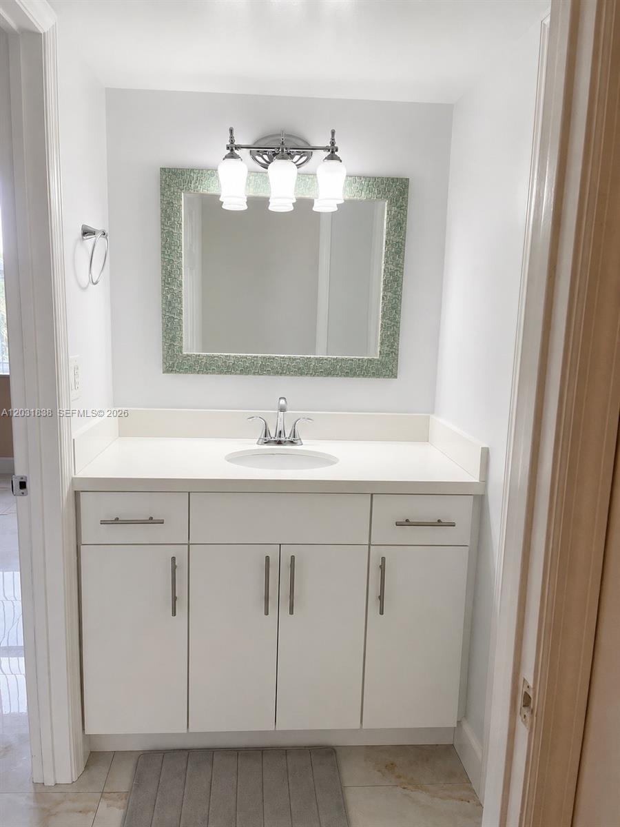 A bathroom vanity features white cabinetry, a white countertop, and a decorative framed mirror — 9420 Tangerine Pl # 401, Davie FL 33324, DAVIE, FL