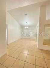 An empty room with vaulted ceilings, beige tile flooring, and a central light fixture — 1551 ORTEGA AVENUE, DELTONA, FL