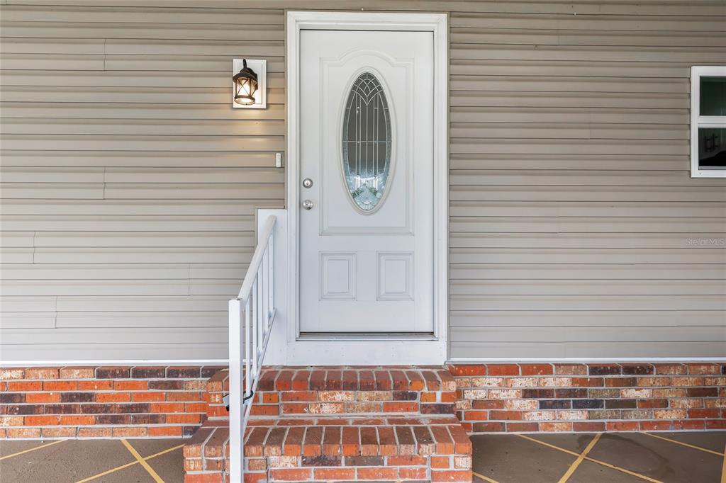 A white front door with an oval glass insert sits above brick steps — 100 PAPAYA COVE, LEESBURG, FL