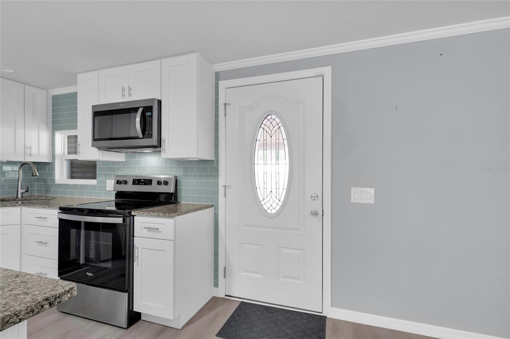 A kitchen features white cabinets, stainless steel appliances, a blue subway tile backsplash, and a door — 100 PAPAYA COVE, LEESBURG, FL
