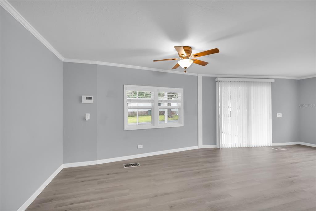 A living room features gray walls, light wood-look flooring, a ceiling fan, and sliding doors — 100 PAPAYA COVE, LEESBURG, FL