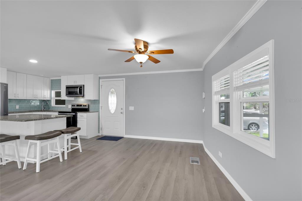 An open-concept kitchen and living area featuring gray flooring, white cabinets, and a ceiling fan — 100 PAPAYA COVE, LEESBURG, FL