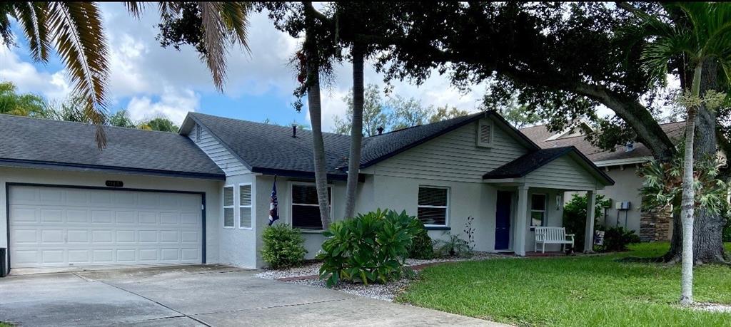 A single-story house with a white garage, gray roof, and a front porch with seating — 915 HARBOR HILL DRIVE, SAFETY HARBOR, FL